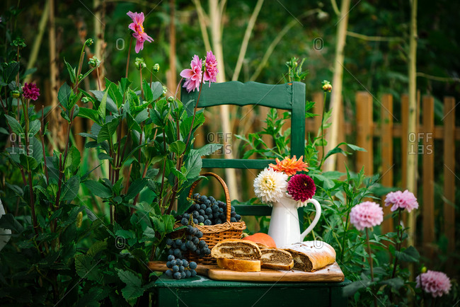 Grapes in a basket beside homemade loaf of bread on a green chair outdoors