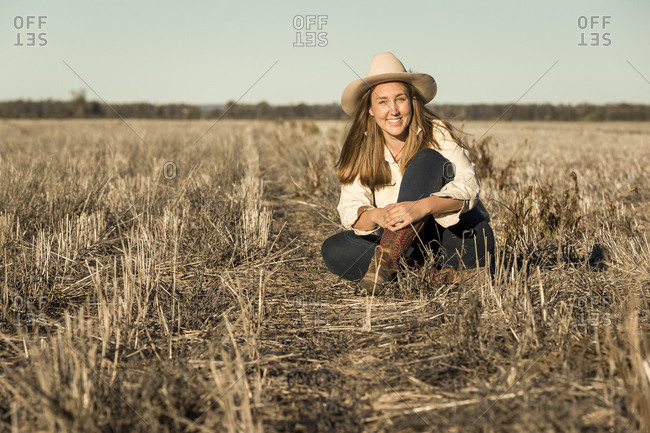 Portrait of a young woman wearing a cowgirl hat sitting in a field