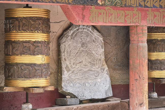 September 6, 2020: Piece of stone with image of Buddha engraved on surface between Tibetan rolls and red shabby columns