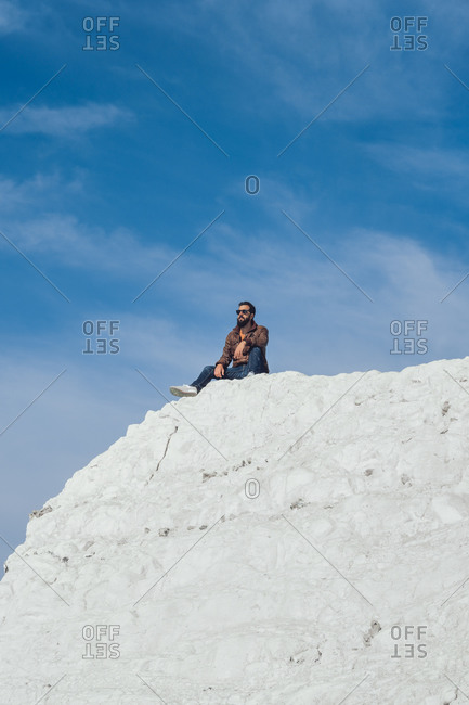From below of unrecognizable male traveler in casual clothes sitting on edge of chalk cliff in Seven Sisters against blue sky