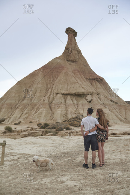 Back view of anonymous young romantic couple hugging and kissing while standing against rocky mountain in Bardenas Reales