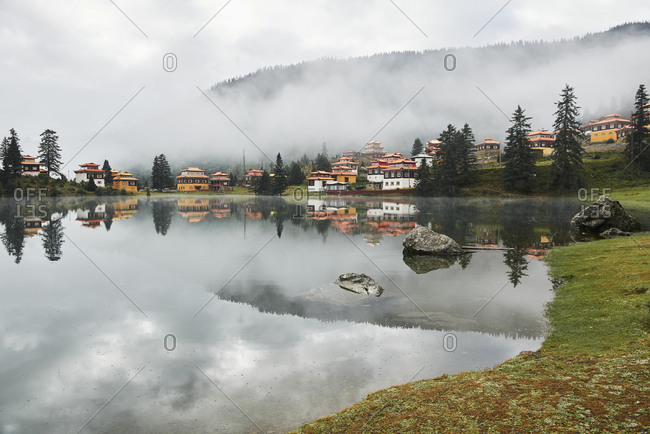 Scenery view of old buildings of Tibetan Buddhist temples located on shore of tranquil reflecting lake in highland covered with clouds