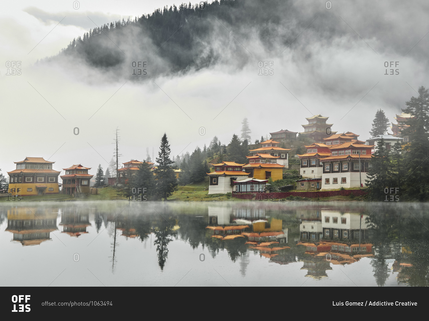 Scenery view of old buildings of Tibetan Buddhist temples\
located on shore of tranquil reflecting lake in highland covered\
with clouds stock photo - OFFSET