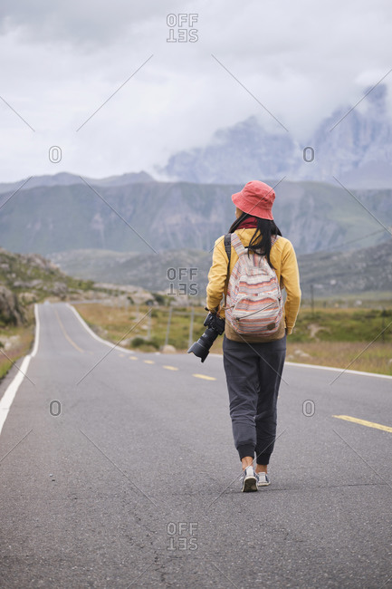 Back view of young Asian female in sportswear strolling on asphalt in picturesque scenery of foggy mountain