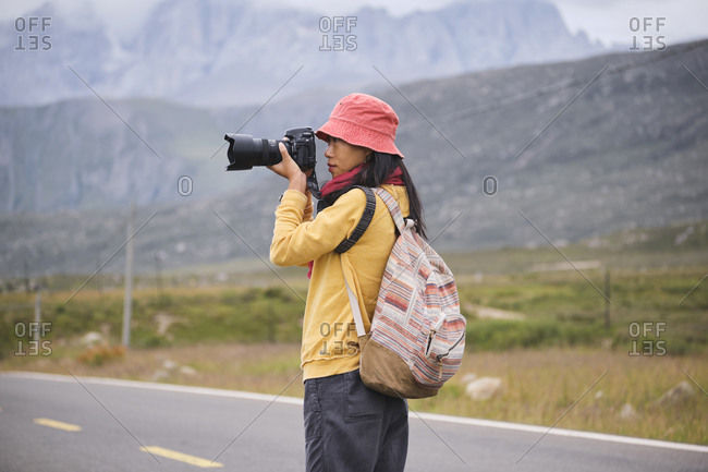 Full body of young Asian female in sportswear strolling on asphalt in picturesque scenery of foggy mountain