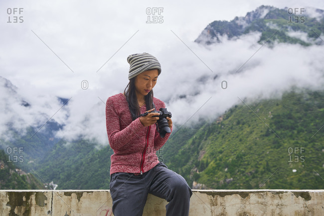 Young Asian female in sporty outfit resting on stone terrace in picturesque foggy green mountains