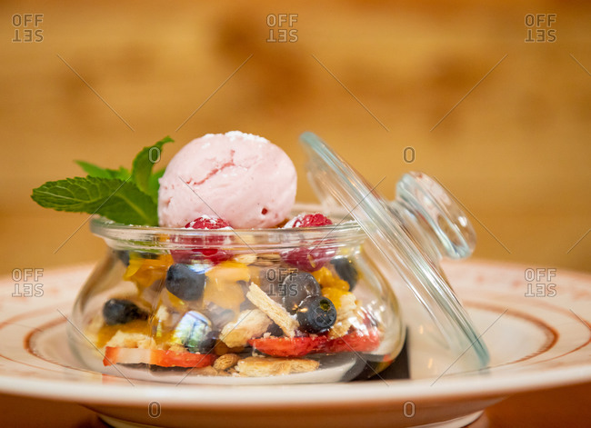 Closeup of delicious scoop of ice cream served in glass jar with various berries and garnished with sprig of mint