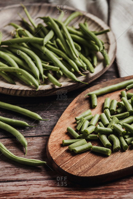 Top view of fresh whole and cut green beans in wooden and metal bowls on linen towel