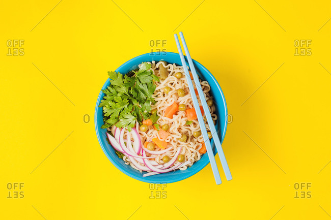 From above of ceramic bowl with appetizing noodles with onion and carrot slices near fresh parsley on top