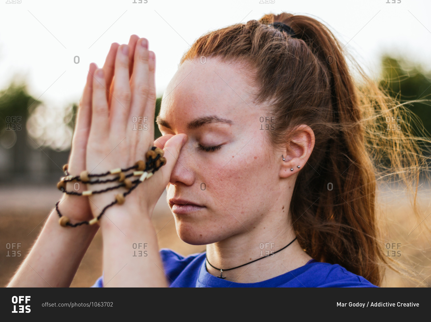 Headshot of tranquil female with Namaste hands with beads meditating with closed eyes at sunset in nature