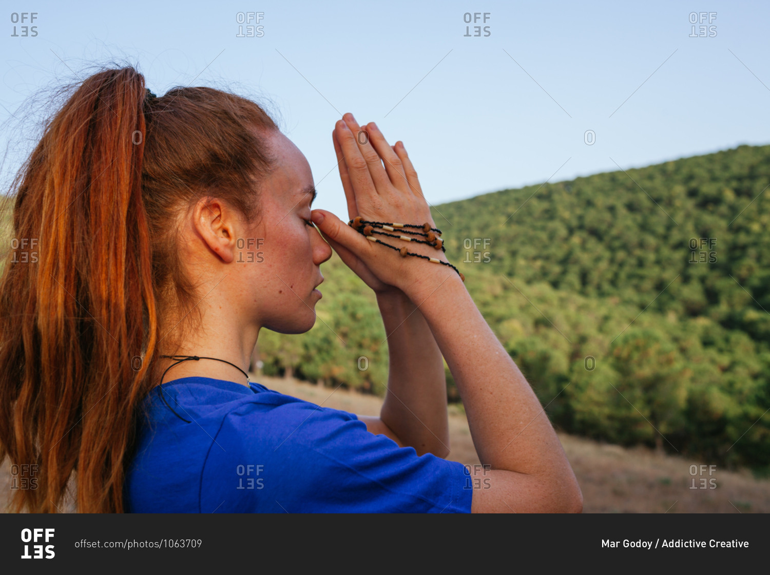 Headshot of tranquil female with Namaste hands with beads meditating with closed eyes at sunset in nature