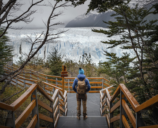 From above back view of unrecognizable hiker in warm clothes with backpack standing on viewpoint and observing picturesque landscape of Perito Moreno glacier during travel in highlands of Argentina
