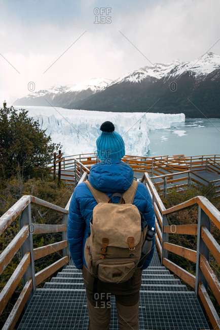 From above back view of unrecognizable hiker in warm clothes with backpack standing on viewpoint and observing picturesque landscape of Perito Moreno glacier during travel in highlands of Argentina