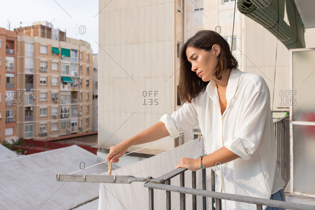 Side view of young female in white shirt and jeans hanging laundry on clothesline on balcony
