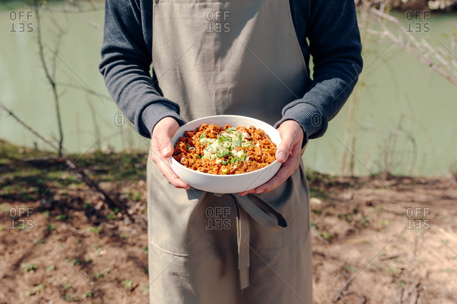 Unrecognizable male cook in apron standing in garden with bowl of delicious minced meat with green onions while preparing rustic meal