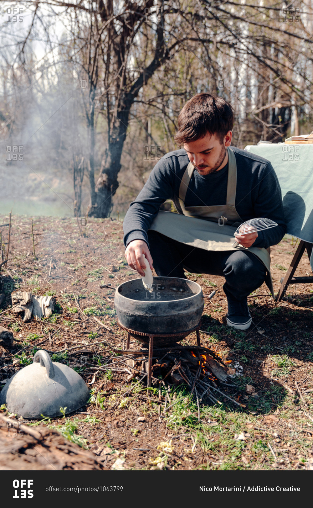 Cook in apron preparing lunch while putting pasty in boiling oil in pot on campfire