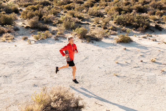 From above of active male jogger running uphill in sandy semi desert terrain during workout in sunny morning