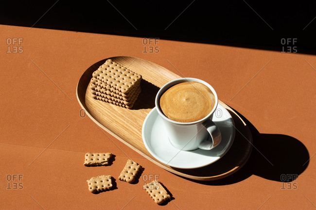 From above of ceramic cup of tasty coffee near crunchy crackers on wooden plate in cafe in sunlight