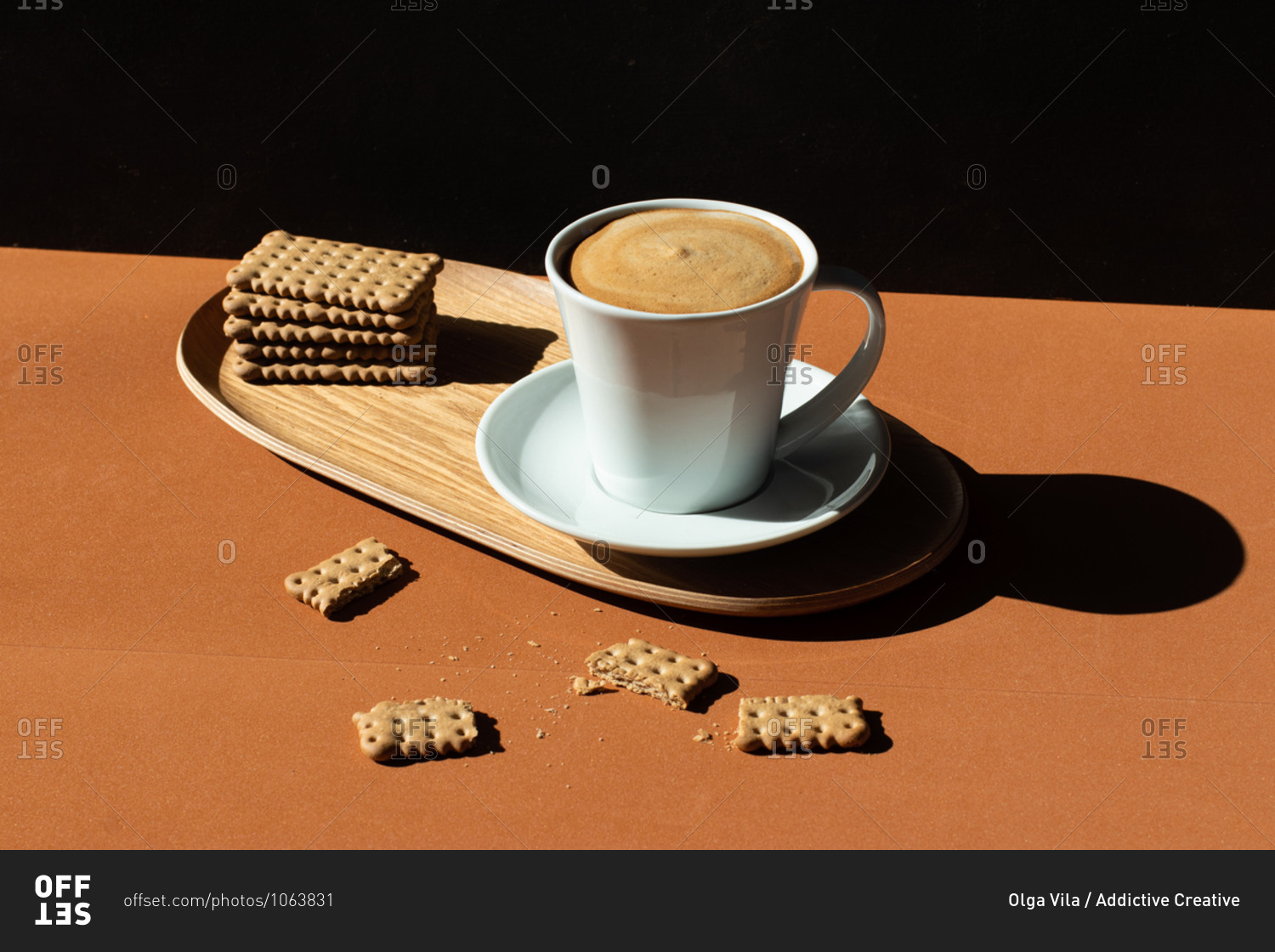 Ceramic cup of tasty coffee near crunchy crackers on wooden plate in cafe in sunlight