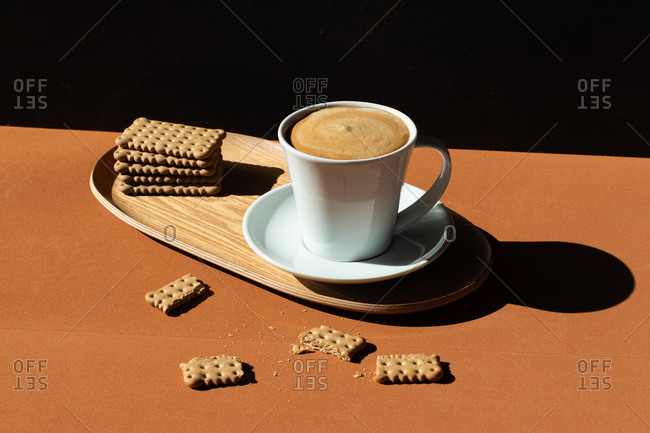 Ceramic cup of tasty coffee near crunchy crackers on wooden plate in cafe in sunlight