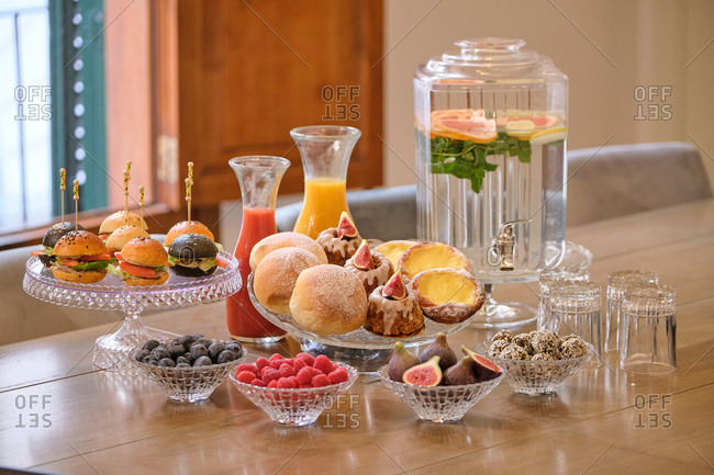 Buffet set with sweet pastry and mini burgers arranged near fresh fruits and berries on table with natural drinks in hotel restaurant