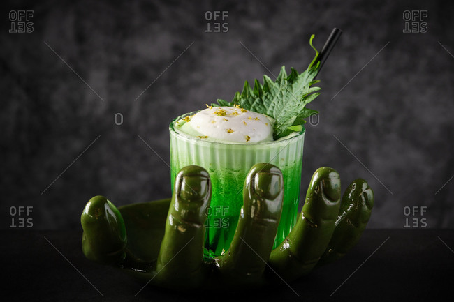High angle glass of refreshing green smoothie with foam and leaf served on creative hand shaped vase