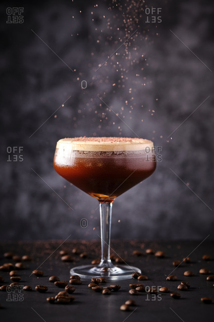 Side view glass of tasty foamy coffee liquor decorated with chocolate and served on black table among scattered beans