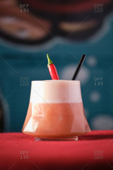 Glass of tasty exotic cocktail with froth served in geometric glass and decorated with chili pepper and straw