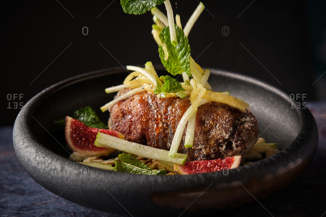 Closeup of unrecognizable cook adding sliced vegetables on palatable pig trotter served on plate with figs in restaurant