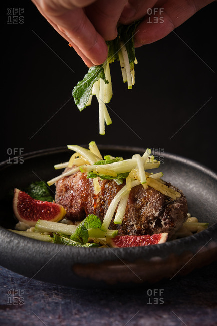 Closeup of unrecognizable chef garnishing delectable pig trotter with fresh greenery at table in kitchen of restaurant