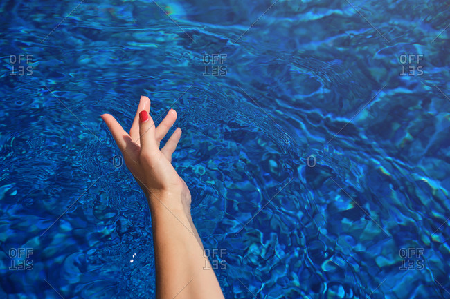 High angle of crop anonymous female traveler with red nails swimming in blue water of pool on sunny day