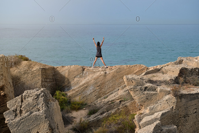 Back view of slim female with hands up observing and enjoying breathtaking scenery of endless ocean