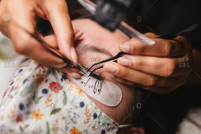 From above of crop anonymous master doing eyelash extension after mapping for unrecognizable female customer in face mask