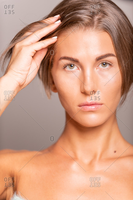 Charming female model with short hair and bare shoulders standing on violet background in studio and smiling at camera