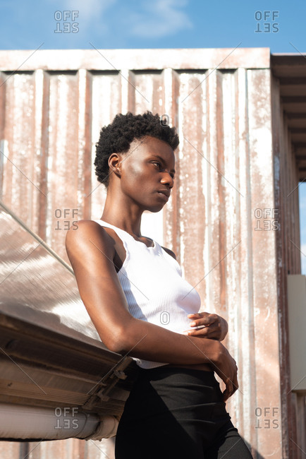 Side view graceful African American female model in white shirt laying back looking away on construction on sunny roof