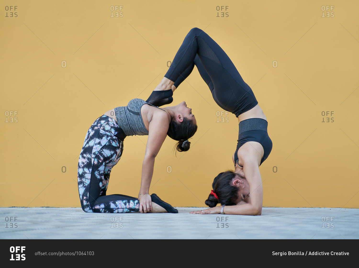 Side view full body fit females in sportswear performing gymnastic acroyoga pose against yellow wall in spacious studio
