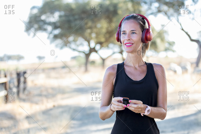 Focused young woman in black shirt using modern MP3 player and listening music in headphones while spending sunny day in park