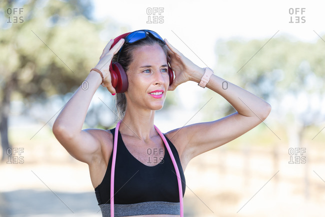 Glad sportswoman with headphones standing in park