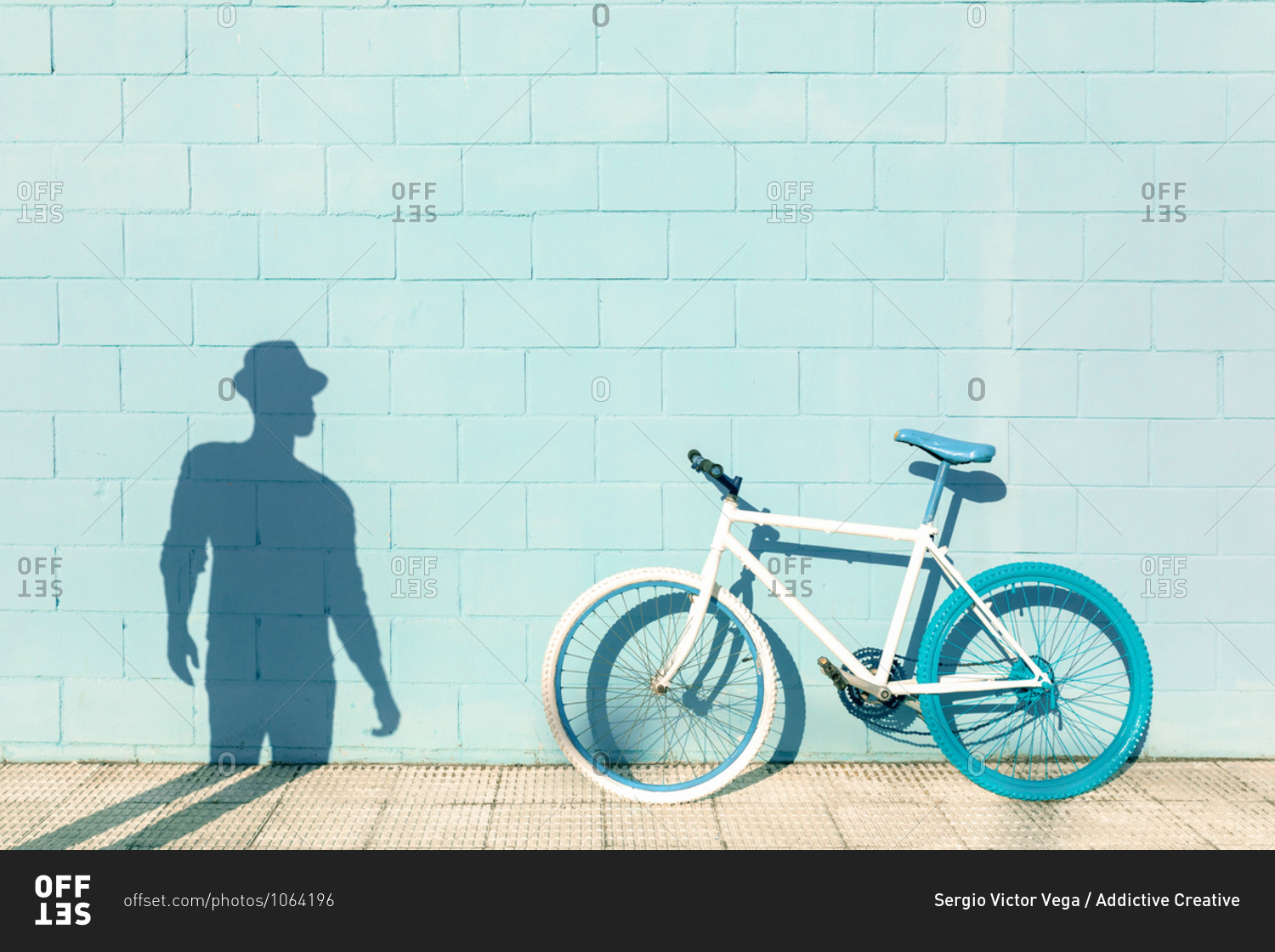 Shadow of unrecognizable man on blue wall near stylish bicycle parked on sidewalk on sunny day