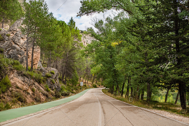 Empty curved asphalt road leading between green forest and mountains in cloudy summer day