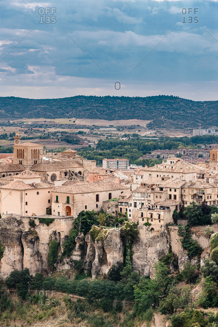 Scenic view of medieval town Cuenca with old stone houses located on hills covered with green trees under blue cloudy sky in summer day in Spain