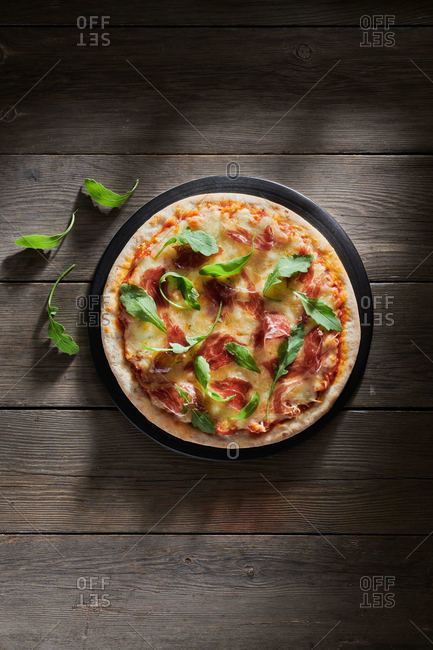 Top view of delicious pizza decorated with fresh basil and arugula leaves