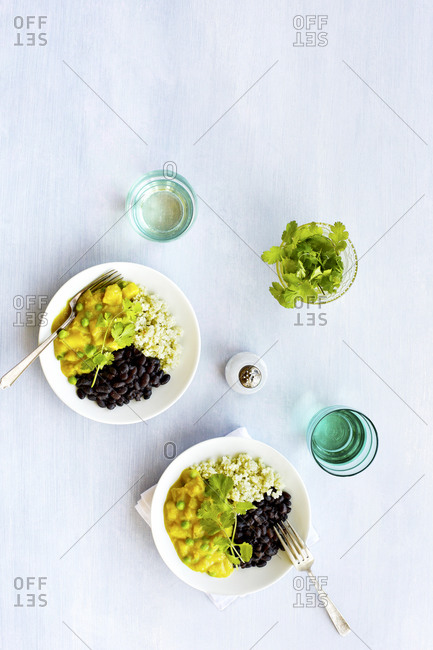 High angle view of potato pea curry with black beans and jade rice on light background