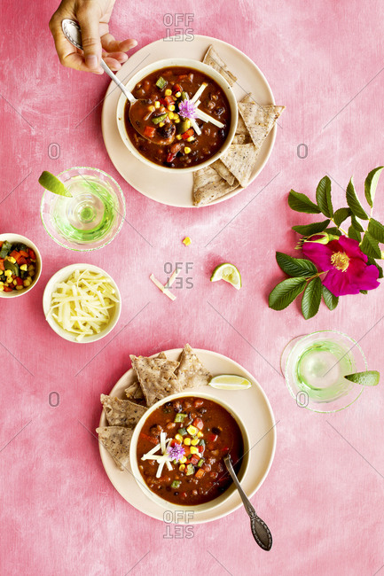 Overhead view of person eating bowls of spicy four bean chili on pink surface