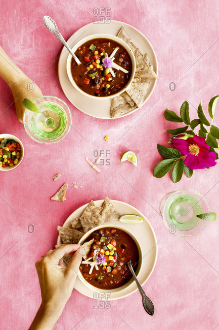 Two people eating spicy four bean chili and drinking cocktails on pink surface