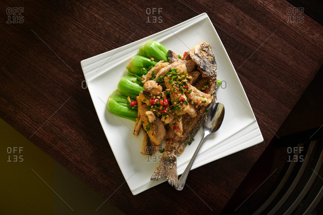 Whole fried sea bass over steamed baby bok choy and covered with stir fried garlic and spicy Thai chiles served in a Chinese restaurant