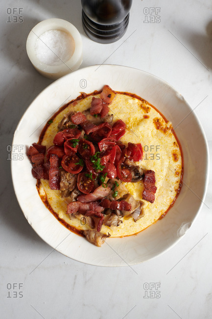 A dish of creamy polenta with bacon, oyster mushrooms, shallots, cherry tomatoes, and green onions in a bowl by sea salt