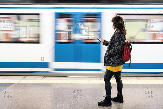 Adult woman wearing face mask due to covid19 using her phone while the metro arrives in Madrid, Spain