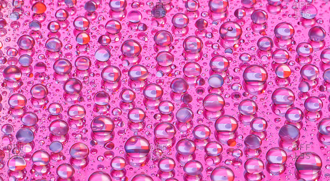 Abstract macro of water droplets on shiny surface with pink cast