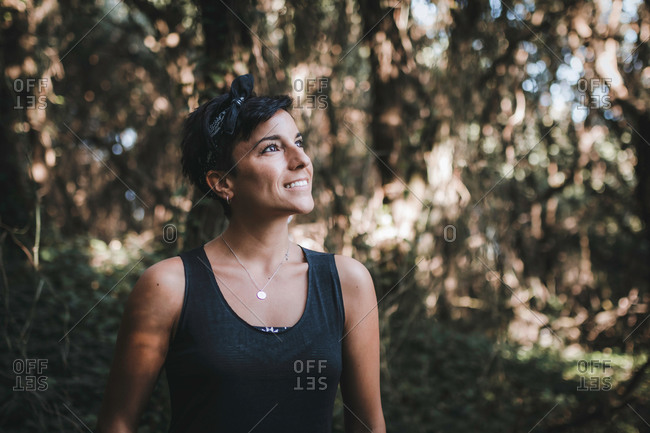 Portrait of a beautiful cheerful woman with short hair and a beautiful smile admiring nature in the forest while hiking in the woods looking up